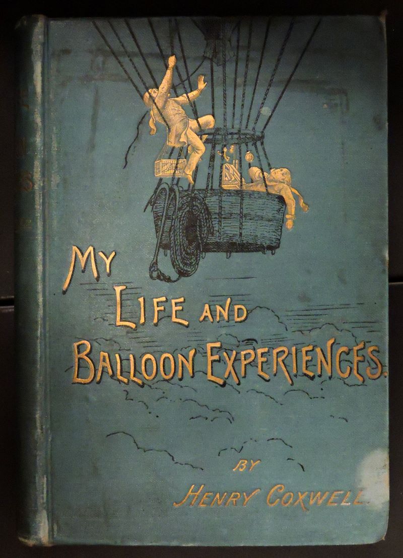 Picture of dull blue book cover showing two men drawn in gilt in a dark blue drawing of a gas balloon basket at high altitude. Title and author is in gilt lettering below the drawing.
